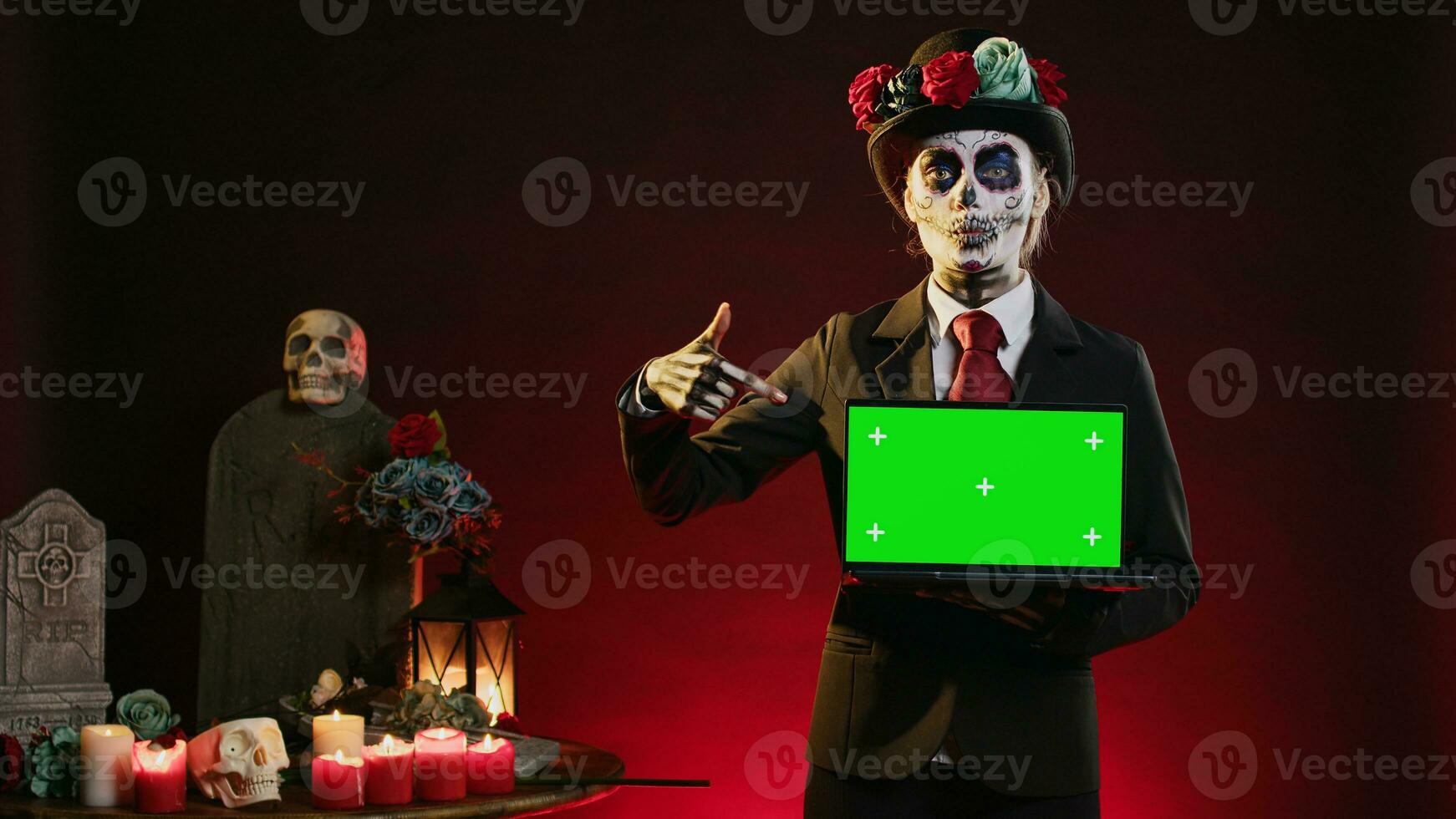 Mexican lady of death showing greenscreen template on laptop, smiling on dios de los muertos. Beautiful woman holding pc with isolated mockup display, chroma key and blank copyspace. photo