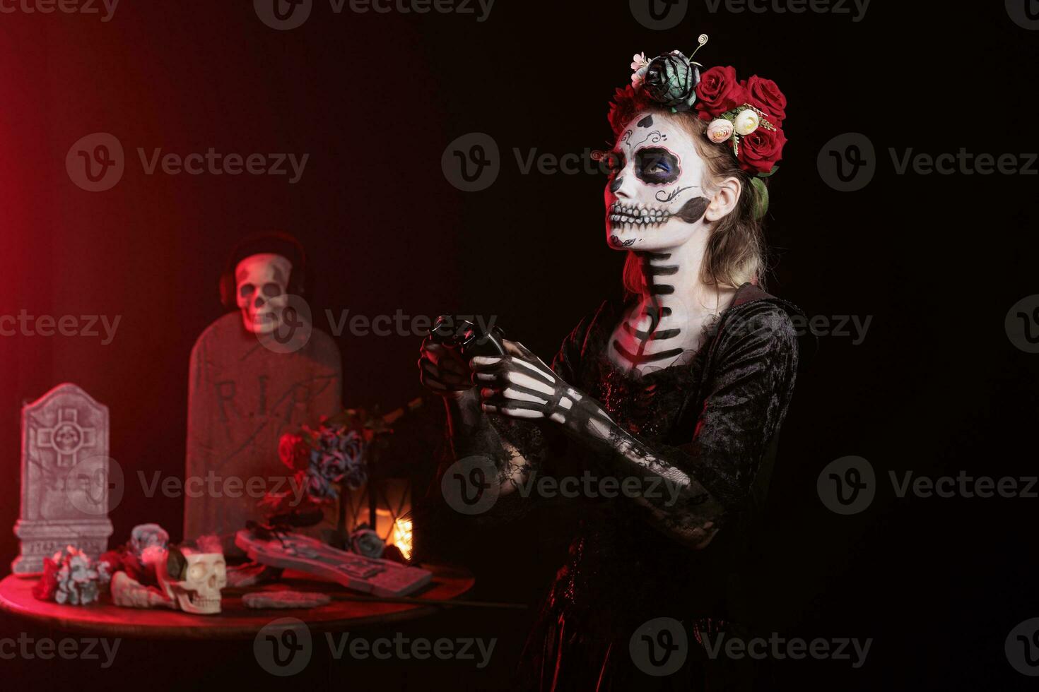 Lady of death model using controller to play video games in studio, playing gaming competition and wearing goddess of death traditional costume. Holding controller and having skull make up. photo