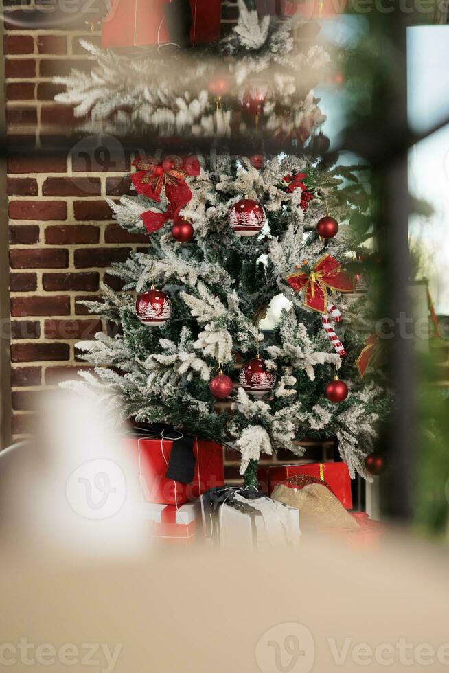 artificial Navidad árbol decorado con rojo adornos detrás ventana en ladrillo pared oficina. festivo hojas perennes con adornos durante nuevo año invierno fiesta temporada en corporativo lugar de trabajo foto