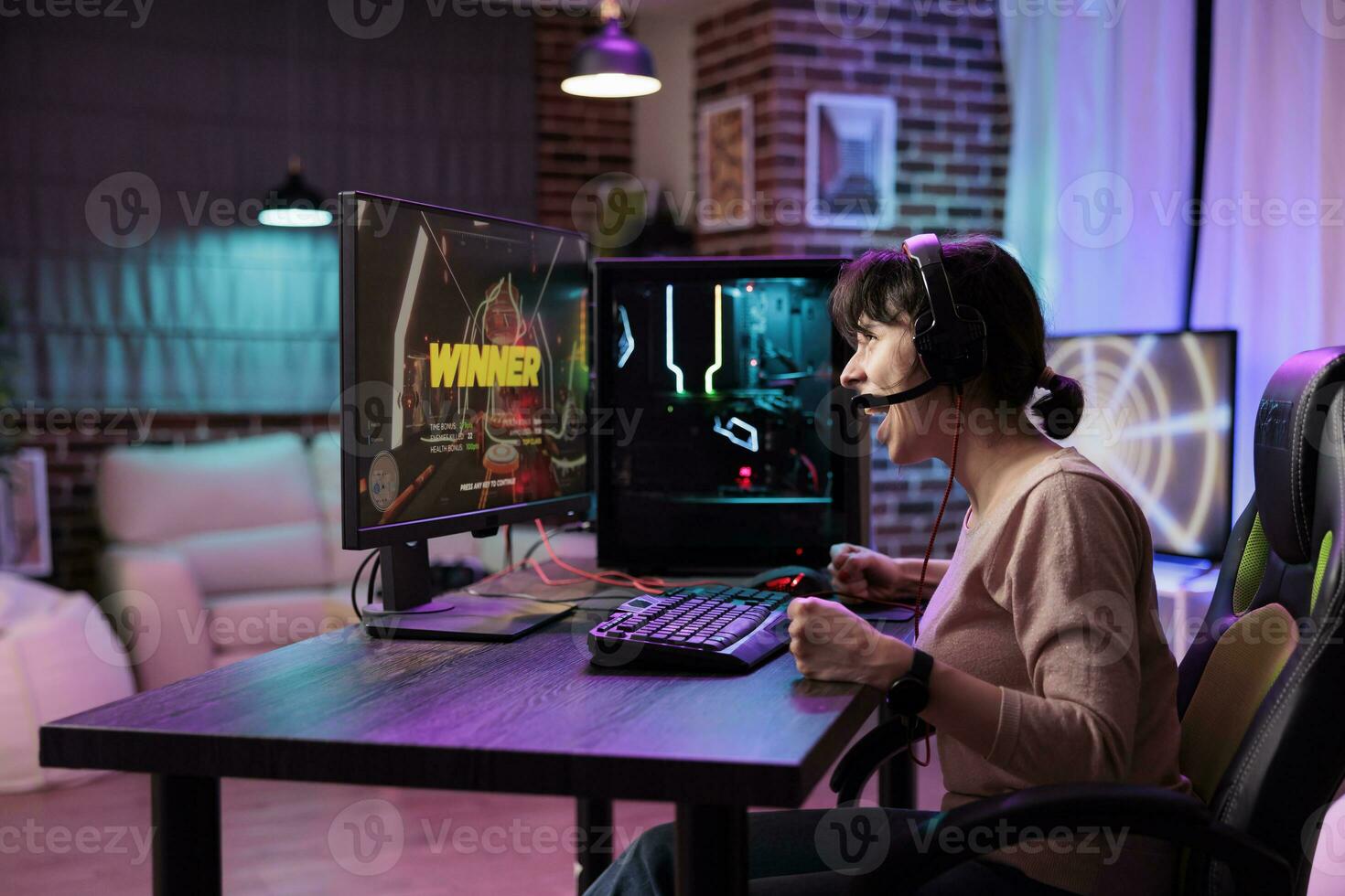 Gamer girl ecstatic after killing opponents in online multiplayer shooting game and winning competition. Woman at computer desk releasing pent up emotions, doing victorious yelling photo