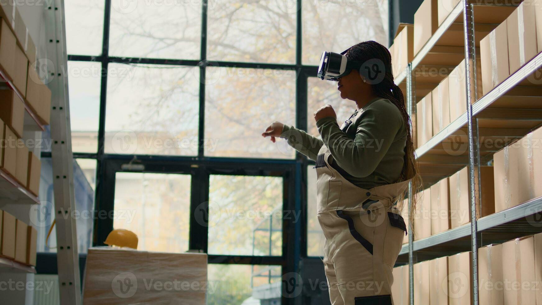 Manager in warehouse wearing VR goggles, using technology to visualize how to best stack cardboard boxes on shelves to make room for more. Supervisor in storage hub uses virtual reality photo