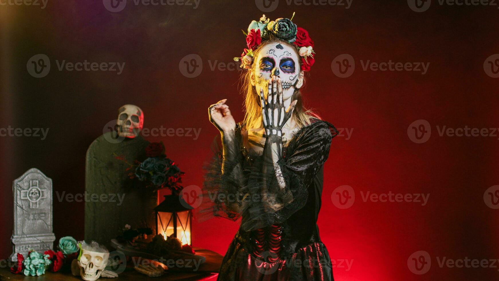 Goddess of death blowing air kisses in studio, acting flirty and romantic with cavalera catrina halloween costume. Doing kissy face with skull body art to celebrate day of teh dead holiday. photo