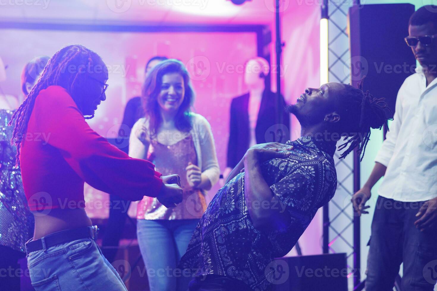 Couple improvising dance battle while clubbing and partying in nightclub. African american man and woman showing moves on dancefloor while having fun at discotheque social gathering photo