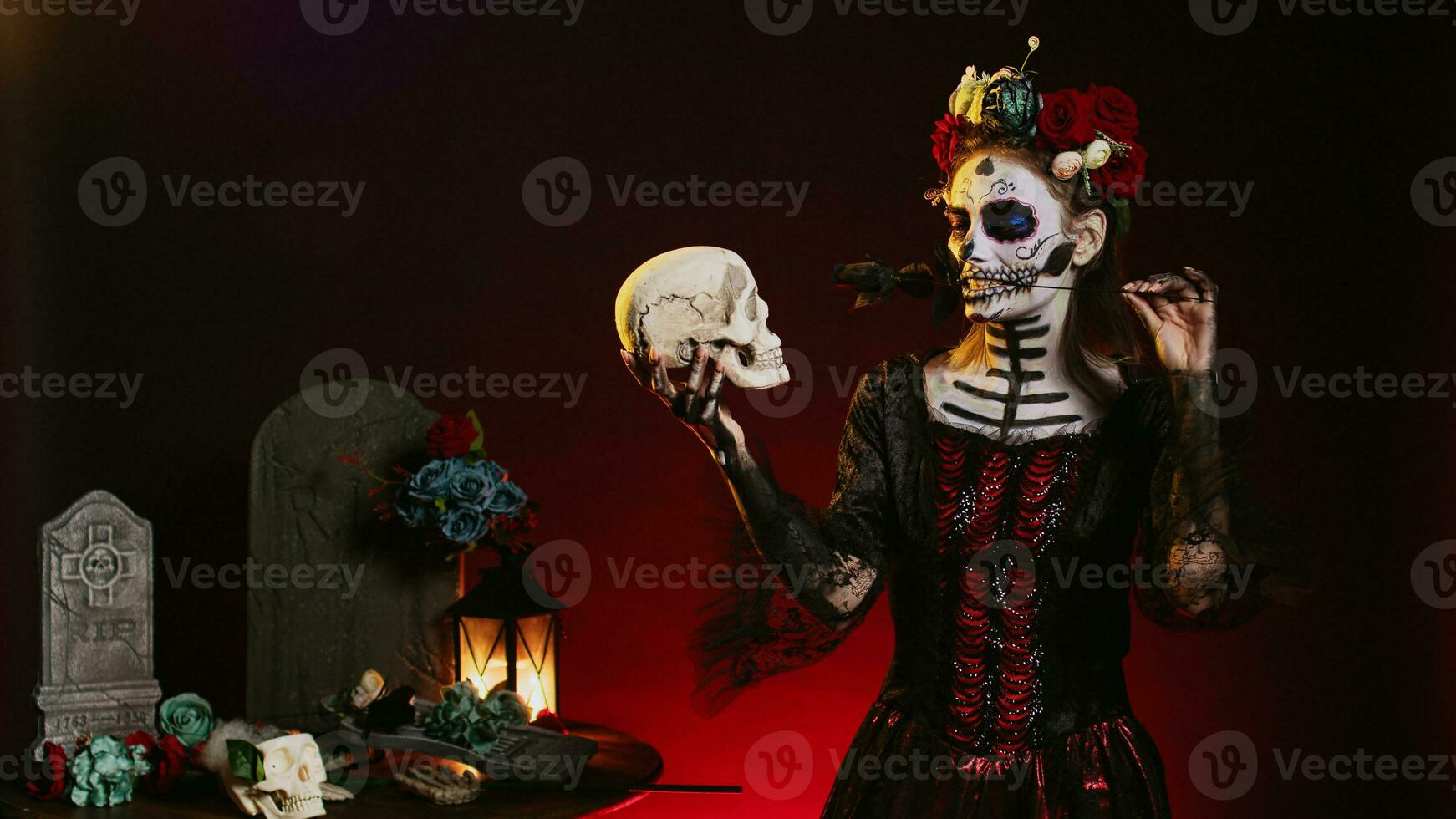 Spooky woman acting creepy with skull in hand, looking at halloween skull. Wearing scary make up looking like santa muerte with flowers crown and body art on holy mexican ritual. photo