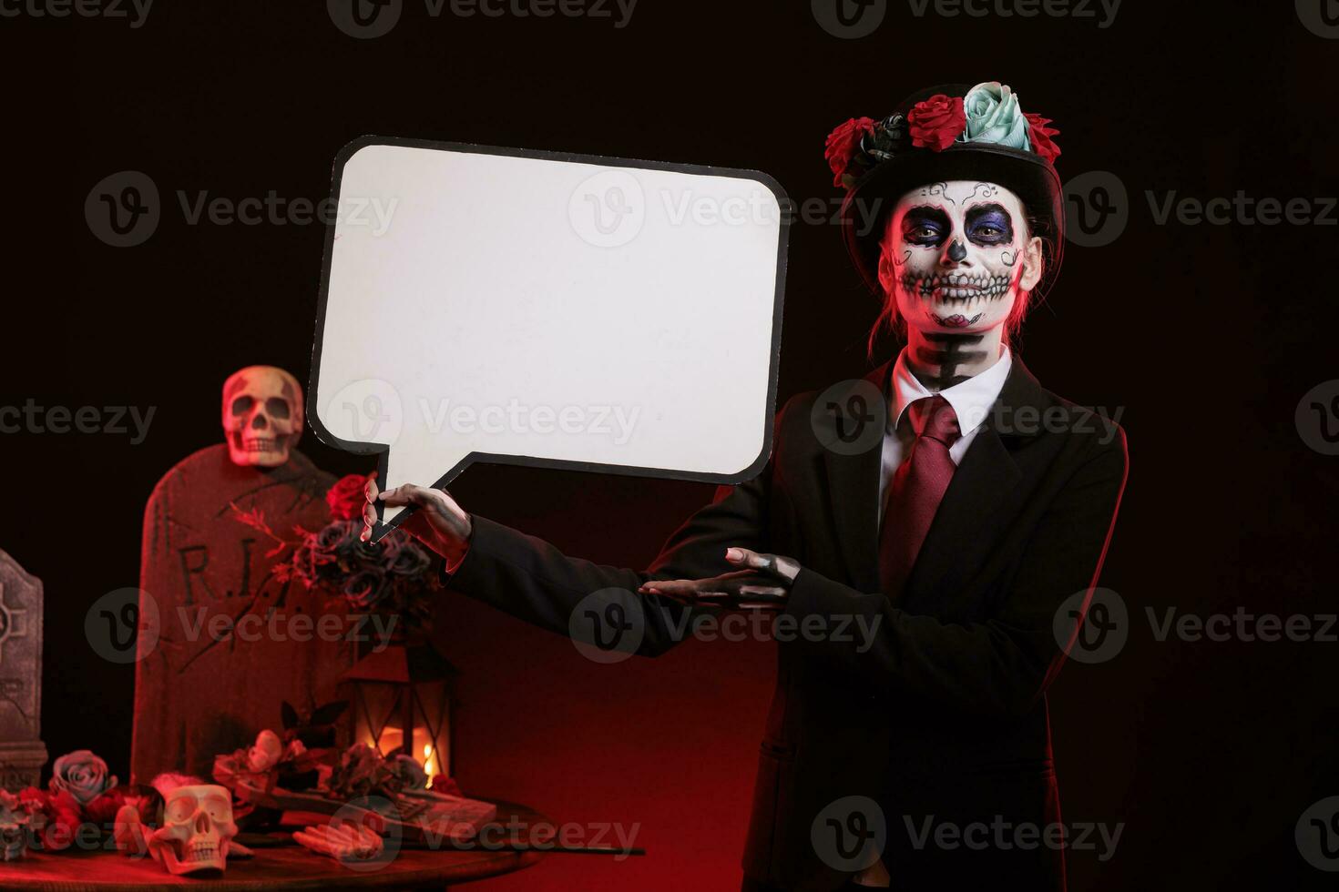 Woman dressed in la cavalera catrina holding speech bubble with carnival make up and traditional day of the dead costume. Advertising isolated mockup cardboard and looking like santa muerte. photo