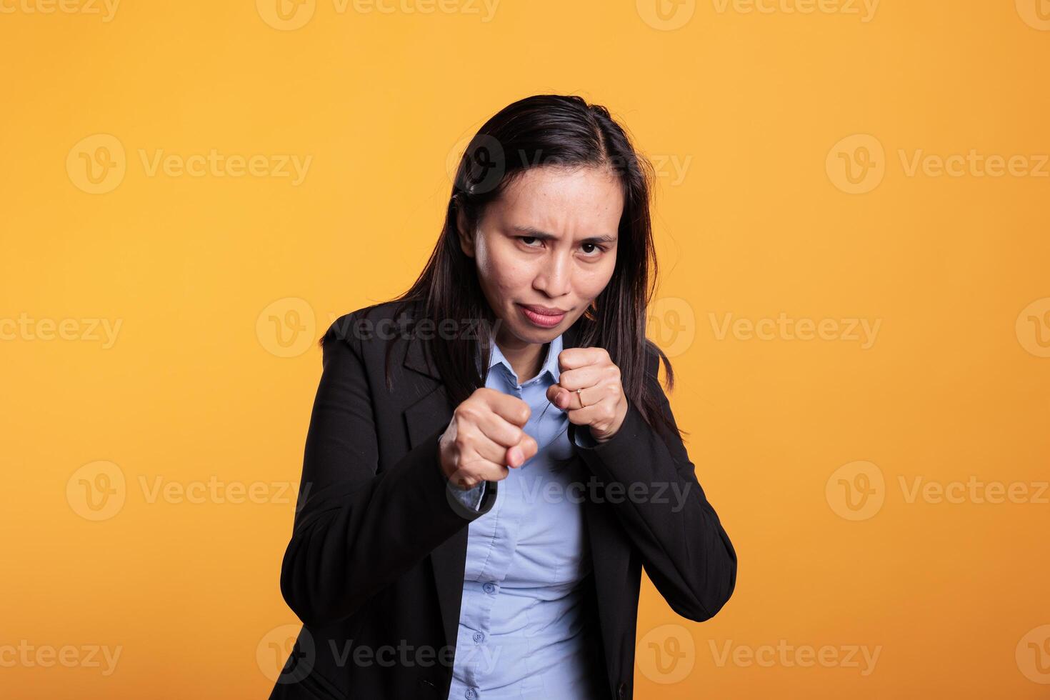 Woman fighter clenching fists to punch in front of camera, preparing for boxing fight in studio. Strong filipino model having angry expression doing fighting gesture, shoowing defense strategy photo