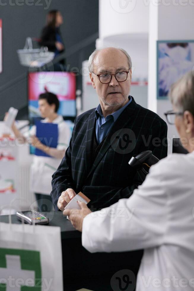 Old man asking pharmacy cashier to scan sunscreen lotion price at apothecary counter desk. Pharmaceutical employee giving assistance service to customer and using scanner on sunblock barcode photo