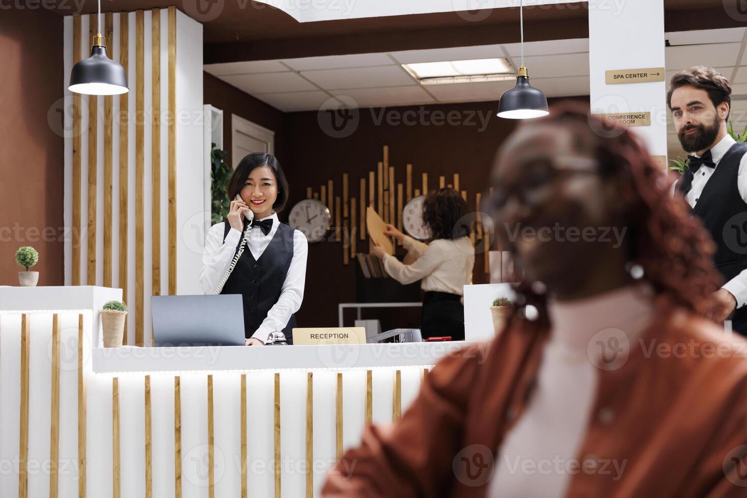 Employee making online room booking on phone, talking on landline call to note room reservation in hotel records. Female reception worker helping future resort guests with accommodation. photo