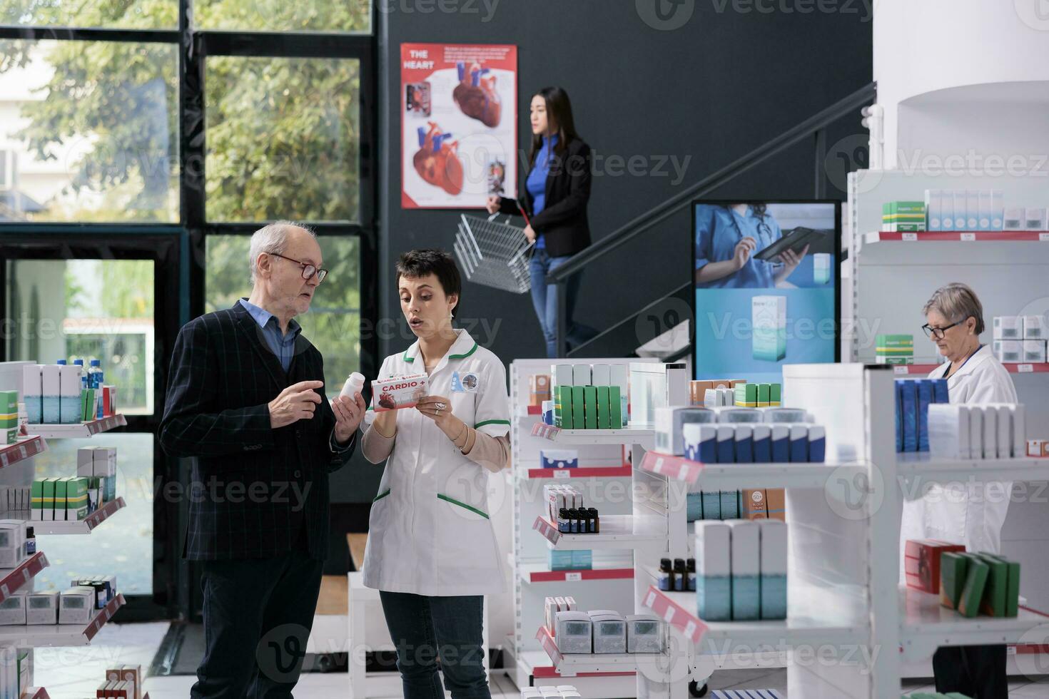 Old customer asking pharmacist to read instruction on medicine package. Pharmaceutical specialist wearing medical uniform explaining buyer pills active ingredients and dosage photo