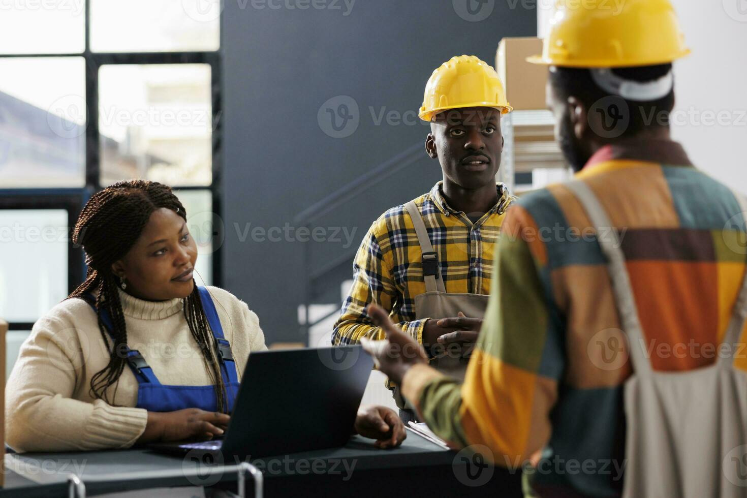 Storehouse managers planning goods inventory at reception counter. African american woman supervisor typing on laptop and listening to warehouse worker explaining parcels storing system photo