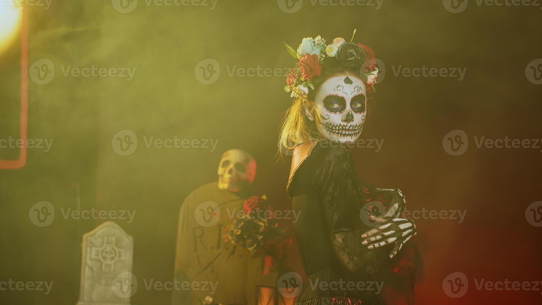 Glamorous woman with sugar skull make up and flowers headband, dressed in goddess of death costume as santa muerte. Dios de los muertos art to celebrate mexican tradition in studio. Handheld shot. photo