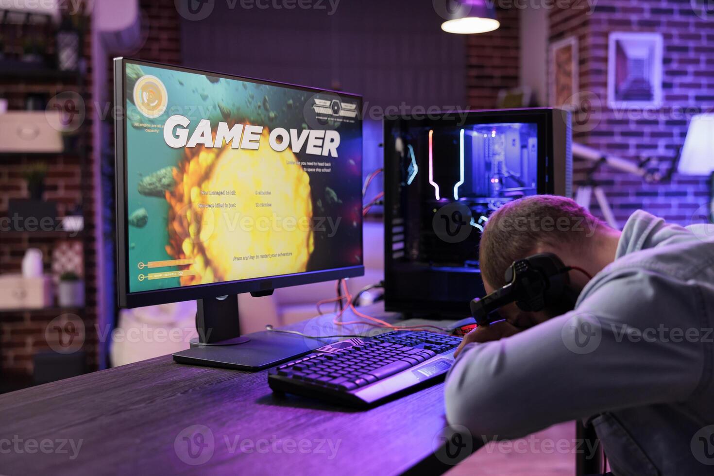 Gamer feeling gutted after losing singleplayer action videogame level, being outsmarted by enemies. Uspet man placing head on desk in frustration after seeing game over screen photo