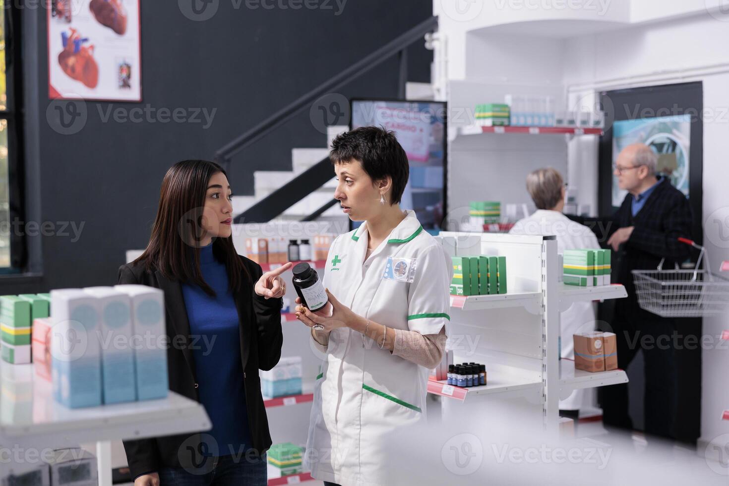 Customer returning vitamin bottle to pharmacist in drugstore, complaining about supplements quality. Young asian woman and confused pharmaceutical assistant talking about multivitamin in apothecary photo