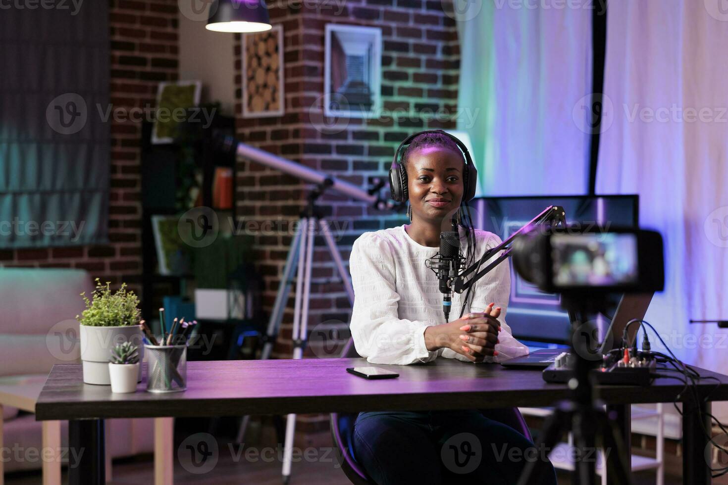 African american vlogger recording internet show using modern camera, talking about history subjects. Influencer filming live broadcast using professional devices in living room studio photo