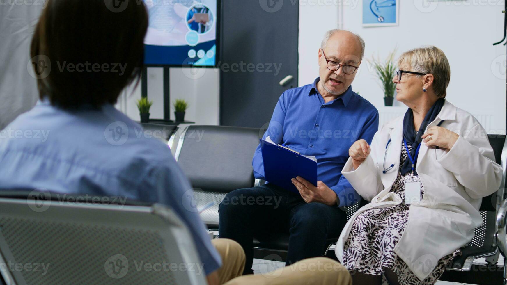 Medic helping patient with medical form in hospital waiting room, discussing health care treatment. Senior man filling insurance documents during checkup visit consultation. Medicine service photo