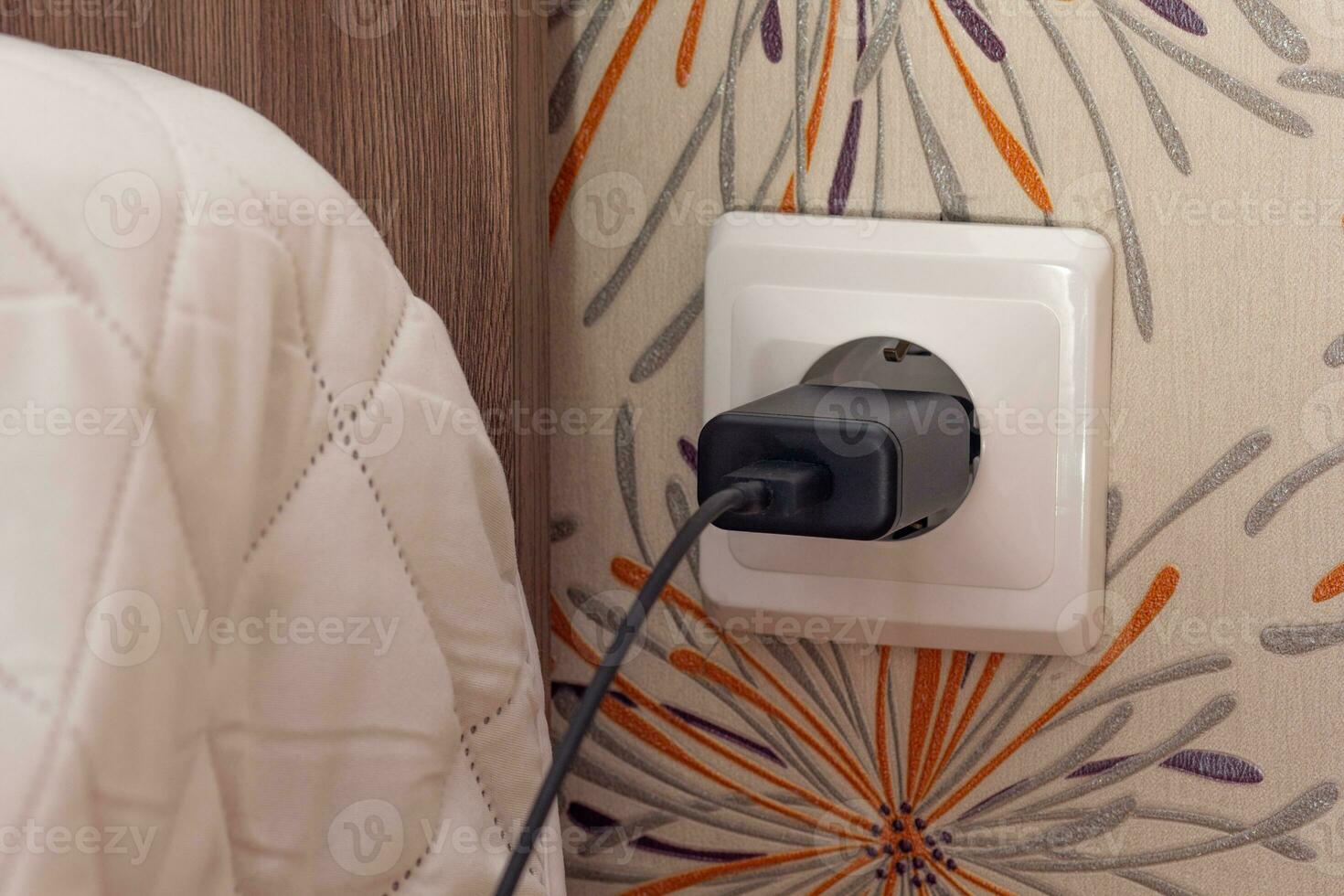 Wall socket with charger plug inside close to bed photo