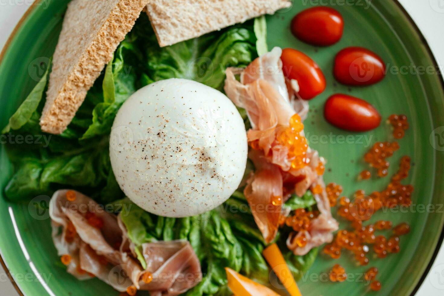 Healthy summer salad with burrata, jamon and tomatoes on green plate. Healthy eating. Portion of fresh gourmet burrata on white background photo
