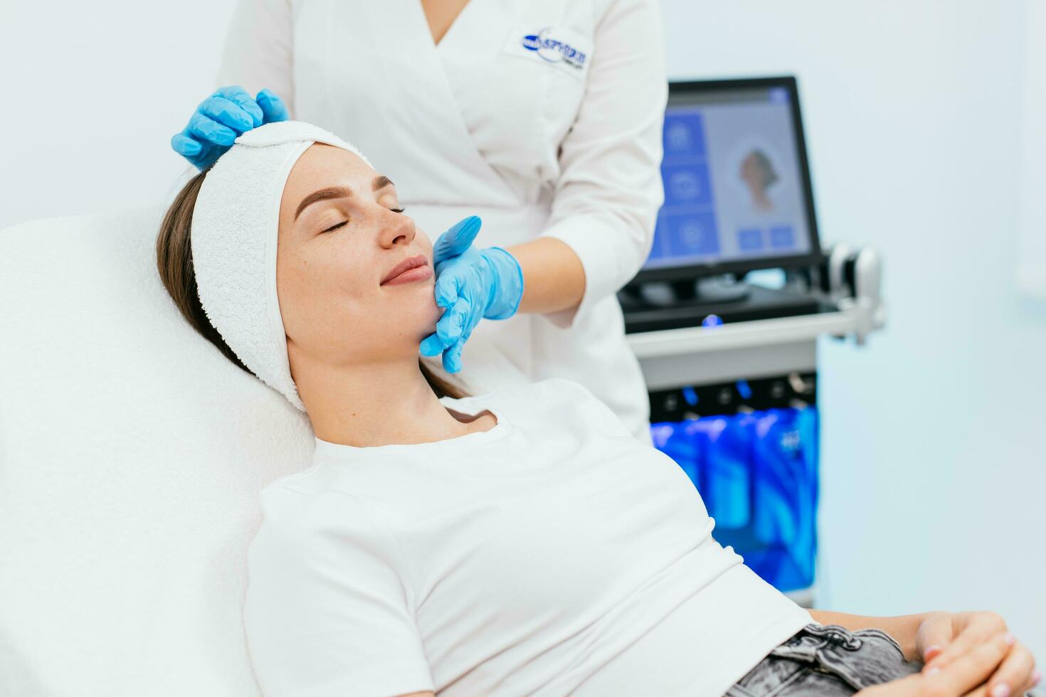 Cosmetology clinic. Professional female cosmetologist doing hydrafacial procedure while being a work. Attractive nice woman lying on the medical bed while having beauty procedures photo