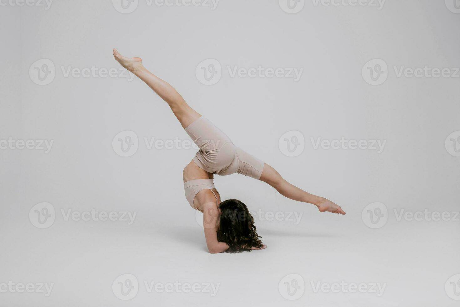 A beautiful slender gymnast in a tracksuit is doing leg split, stretching, yoga in a white studio. photo