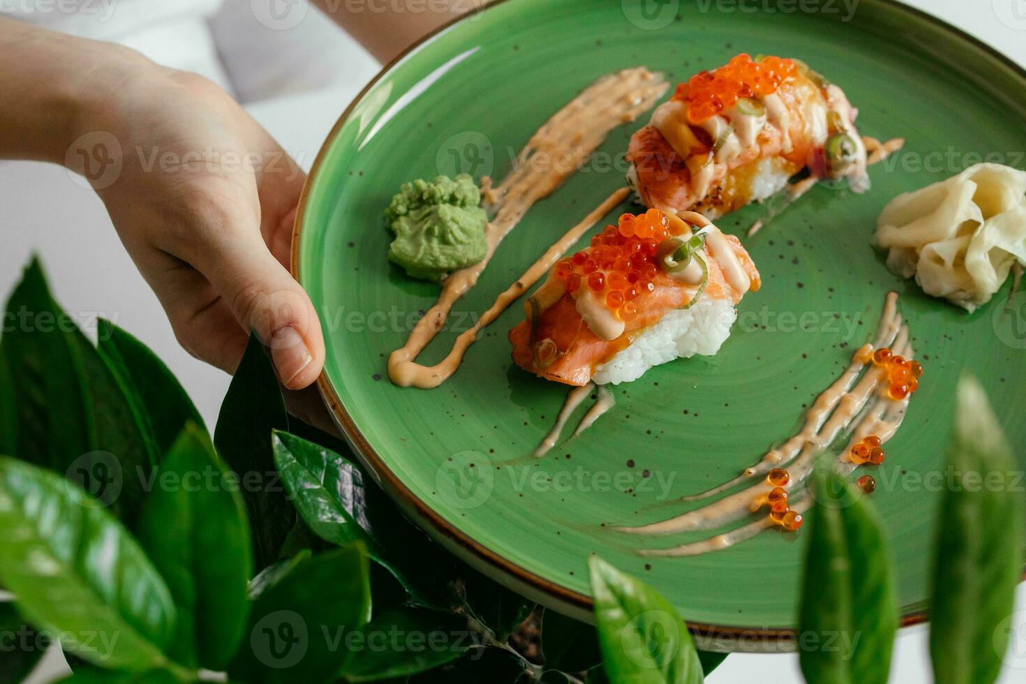 Eating sushi rolls. Japanese food restaurant, salmon maki, gunkan on green plate. Closeup of hand holding plate nigiri rolls. Ginger, wasabi dish photo