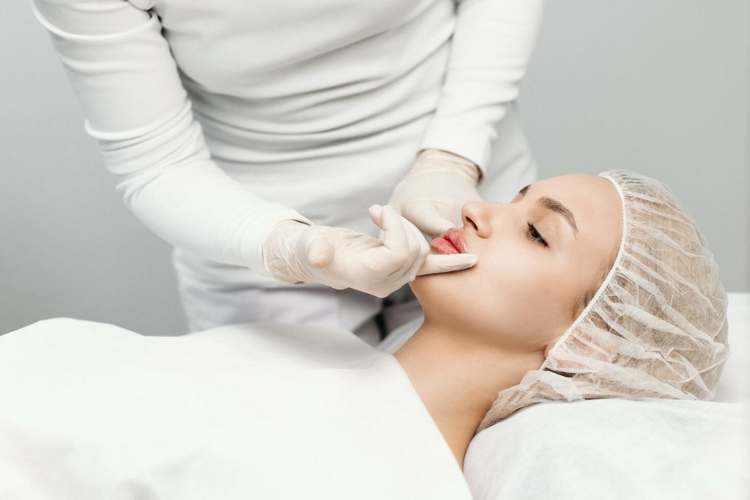 el cosmetóloga hace marcas en el del paciente rostro, dibujo corrección líneas antes de el facial contorneado procedimiento o el plastico cirugía. preparación hora para cosmético tratamiento. foto