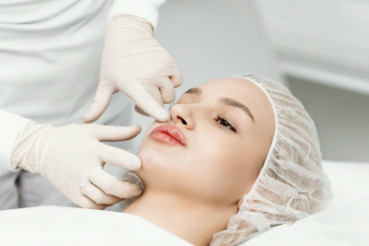 el cosmetóloga hace marcas en el del paciente rostro, dibujo corrección líneas antes de el facial contorneado procedimiento o el plastico cirugía. preparación hora para cosmético tratamiento. foto