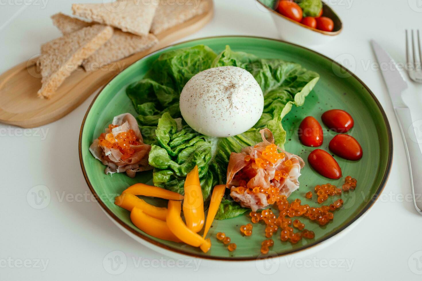 Healthy summer salad with burrata, jamon and tomatoes on green plate. Healthy eating. Portion of fresh gourmet burrata on white background photo