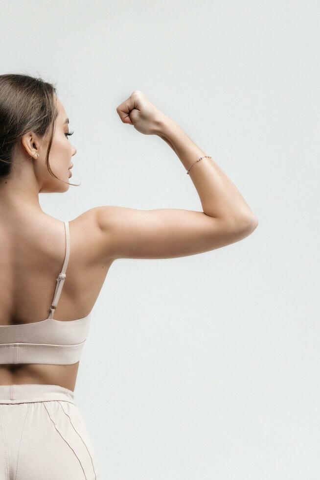 un hermosa deportivo hembra en un tramo en un chandal haciendo deporte, yoga, muestra músculos en blanco antecedentes foto