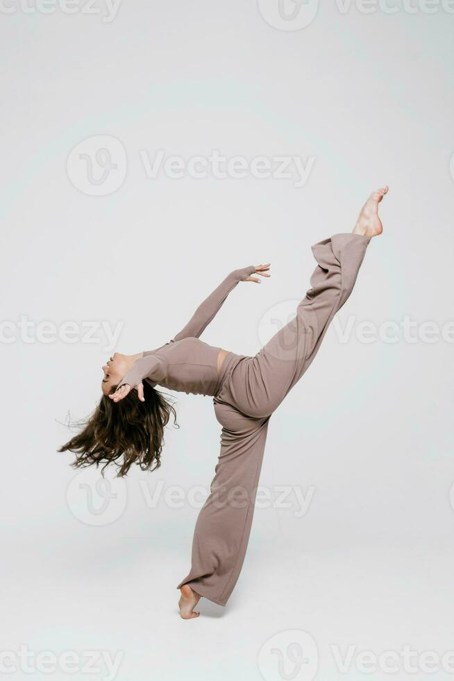 un hermosa esbelto gimnasta en un chandal es haciendo pierna dividir, extensión, yoga en un blanco estudio. foto