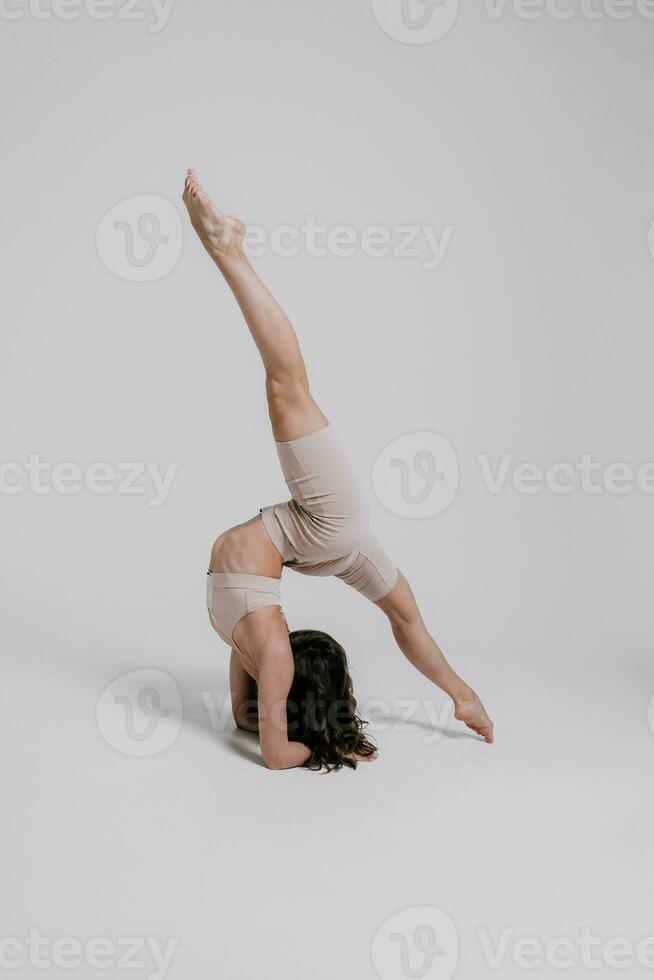 A beautiful slender gymnast in a tracksuit is doing leg split, stretching, yoga in a white studio. photo
