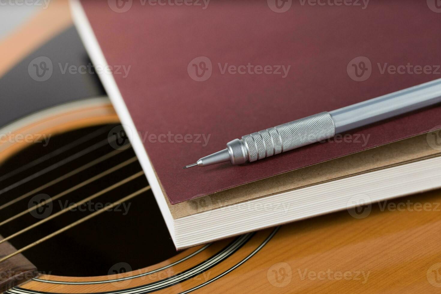 Pencil and notebook placed on acoustic guitar. photo