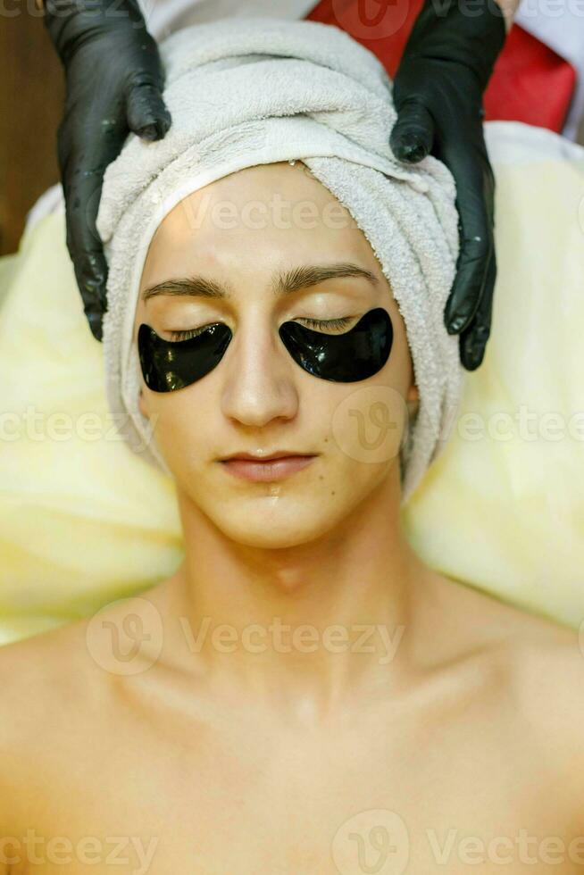 The cosmetologist puts a mask on the face of a young man. photo