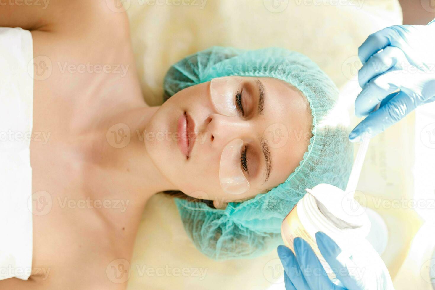 Female cosmetologist making cosmetic facial mask to the female client photo