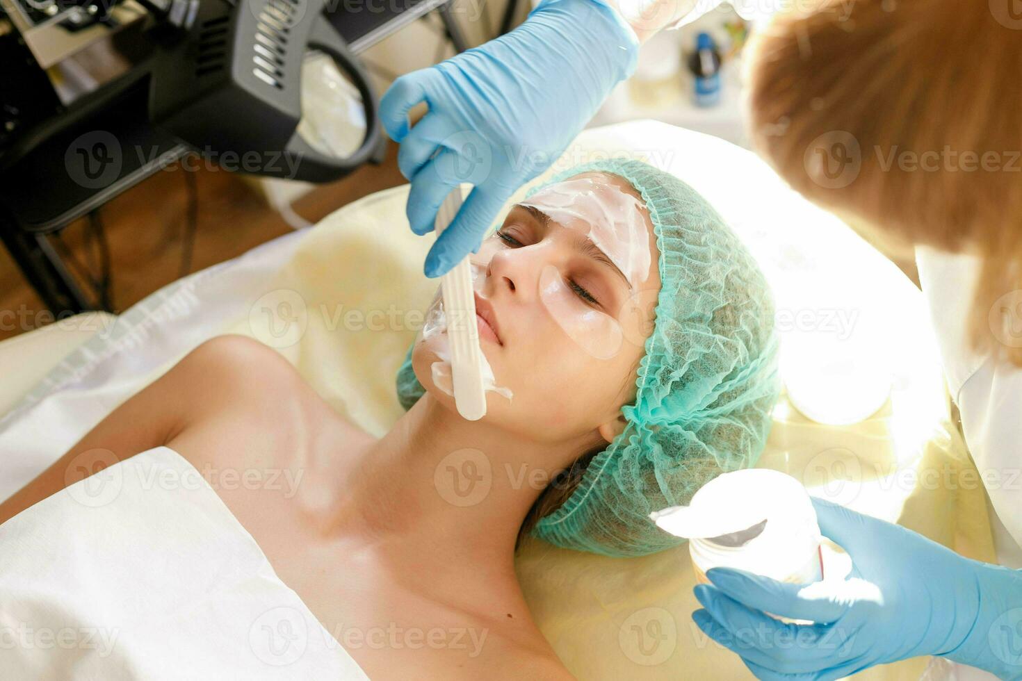 Female cosmetologist making cosmetic facial mask to the female client photo