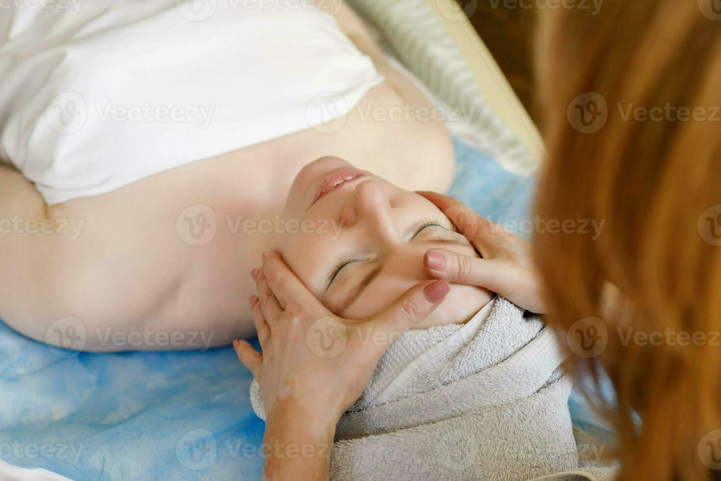 Beautiful young woman receiving facial massage with closed eyes in a spa salon photo