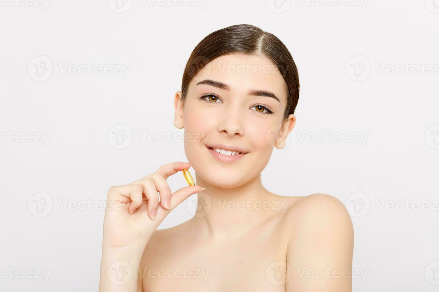 Beautiful smiling young woman holding a fish oil pill in her hand photo