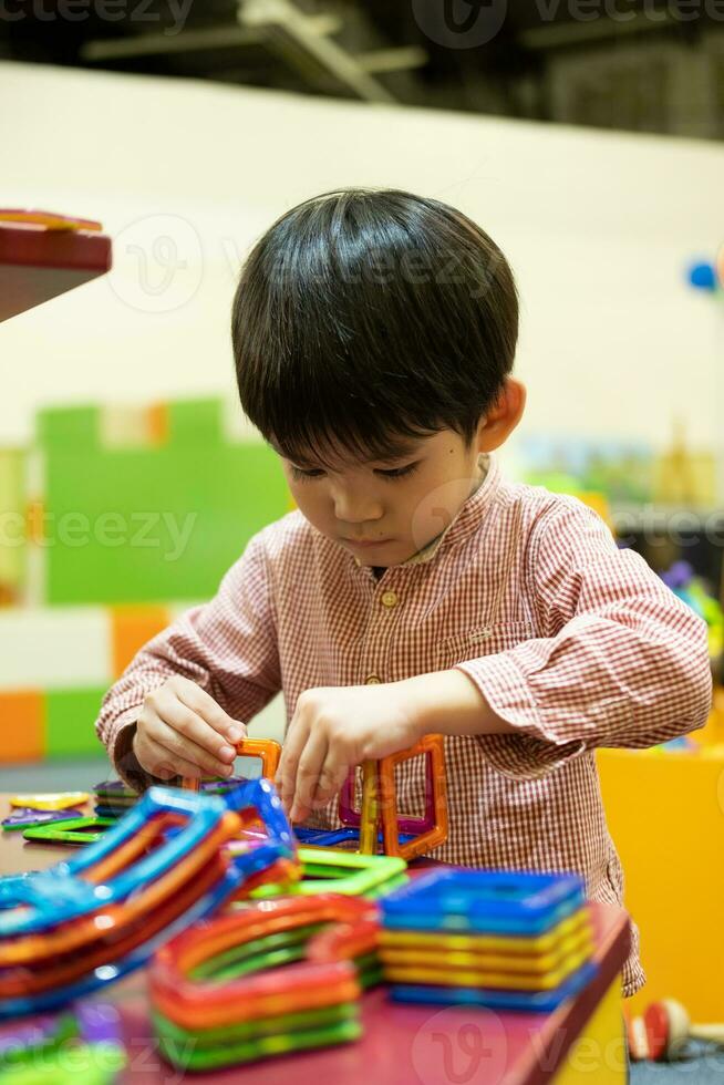 A little Asian boy is playing with a square magnetic puzzle. photo