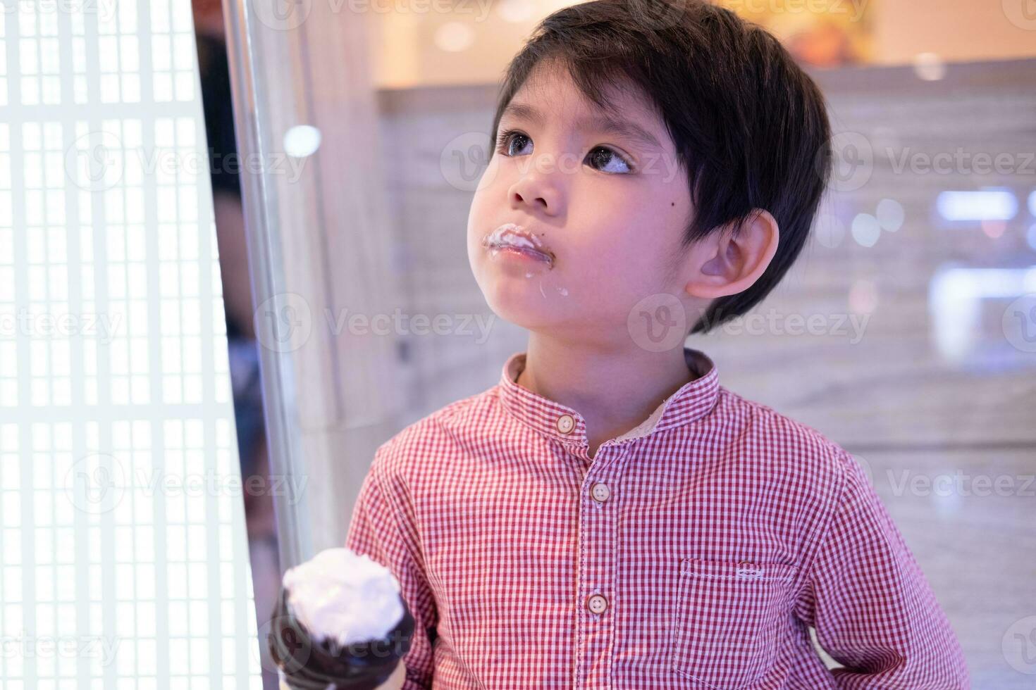 Little Asian boy eating delicious chocolate ice cream photo