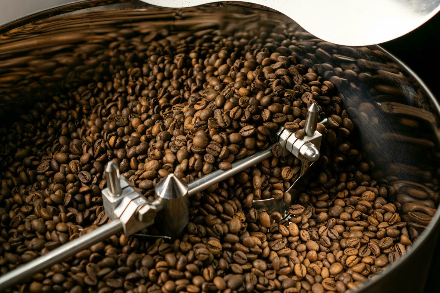 Roasted coffee beans in coffee roaster machine cooling tray. Dark brown roast coffee beans mixed and stirred in coffee roastery machine cooling tray. photo