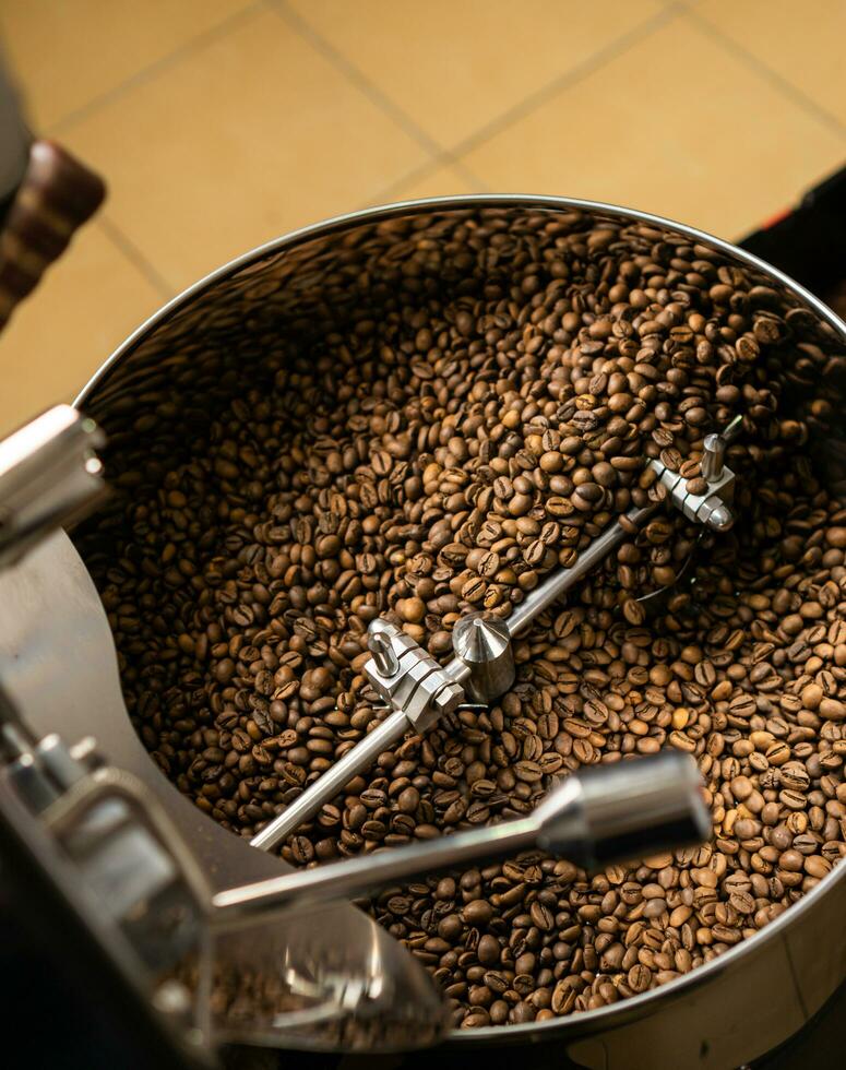 Roasted coffee beans in coffee roaster machine cooling tray. Dark brown roast coffee beans mixed and stirred in coffee roastery machine cooling tray. photo