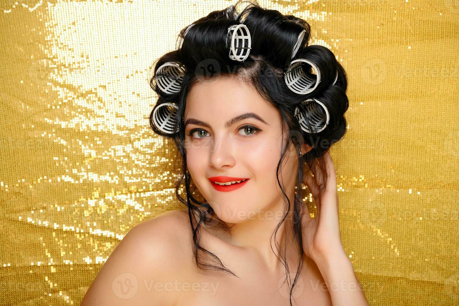 Beautiful girl in hair curlers isolated on gold photo