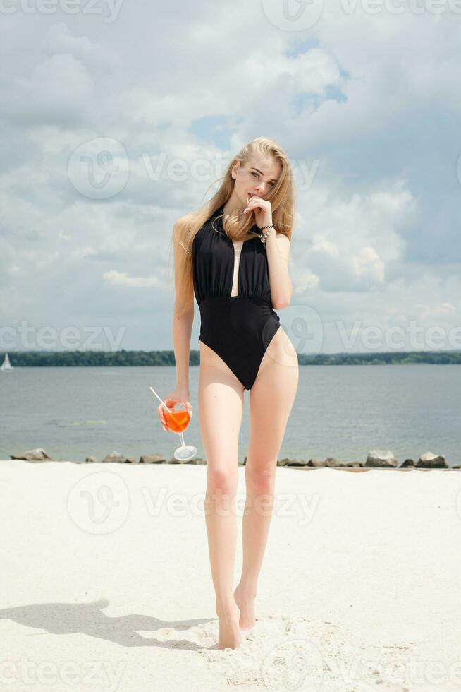 Young cheerful woman in swimsuit, toasting with cocktail, drinking fresh photo