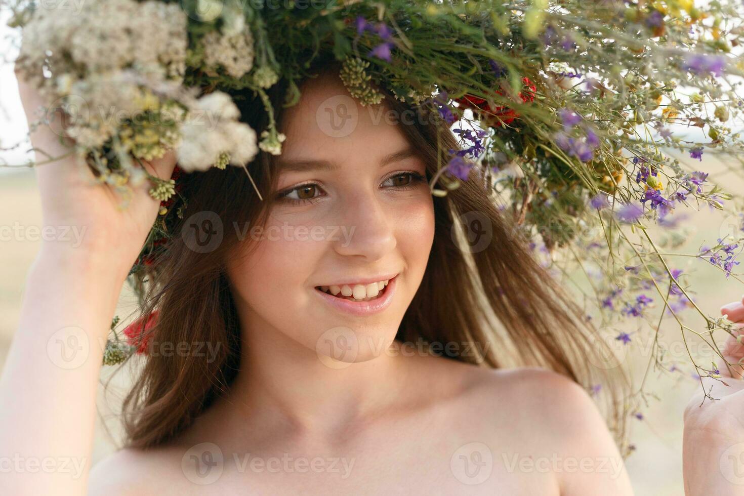 beautiful woman with a wreath on her head sitting in a field in flowers photo