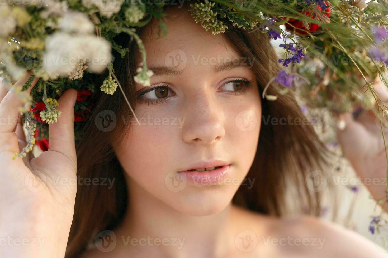 beautiful woman with a wreath on her head sitting in a field in flowers photo