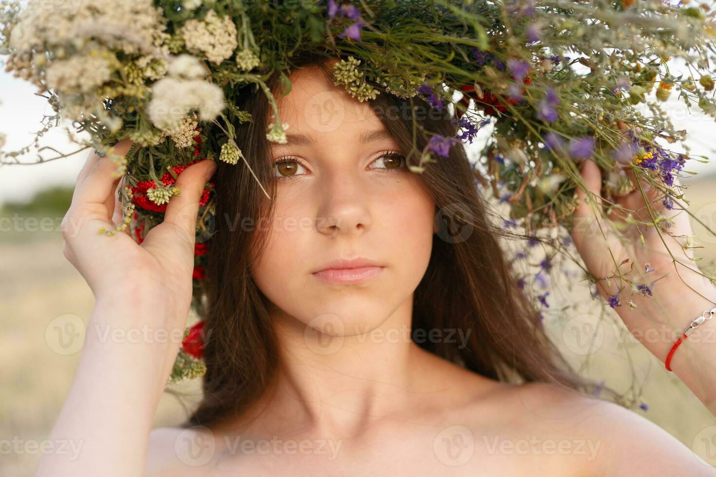 hermosa mujer con un guirnalda en su cabeza sentado en un campo en flores foto