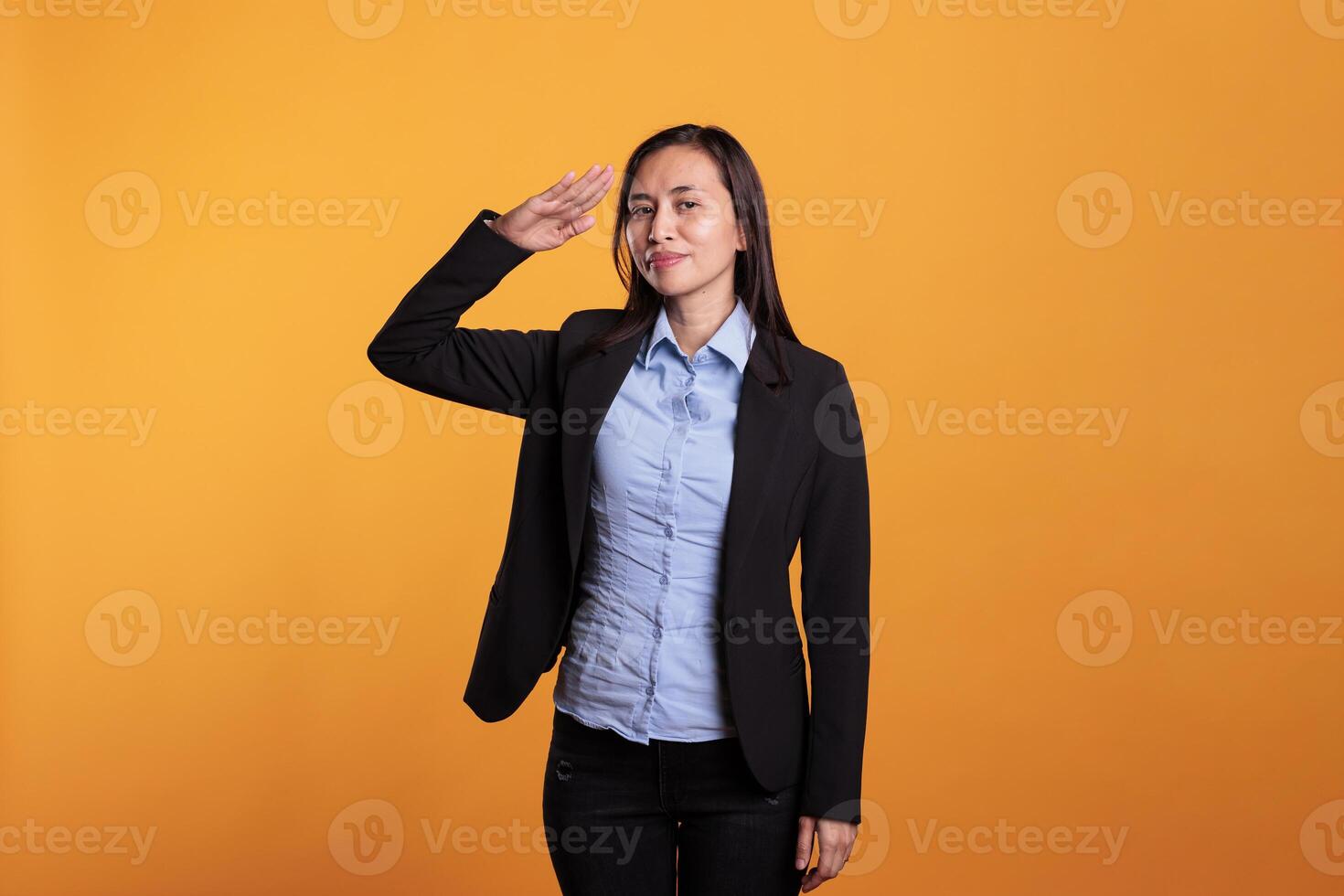 Patriot filipino woman doing military salute with hand over forehead, promotiing honor and respect in front of camera over yellow background Proud adult showing army soldier hello gesture photo