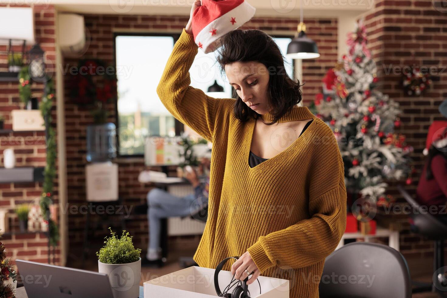 Upset women worker taking off santa hat and packing office things into box after getting fired from job on xmas eve. Unemployed person discharged from work before christmas holiday photo