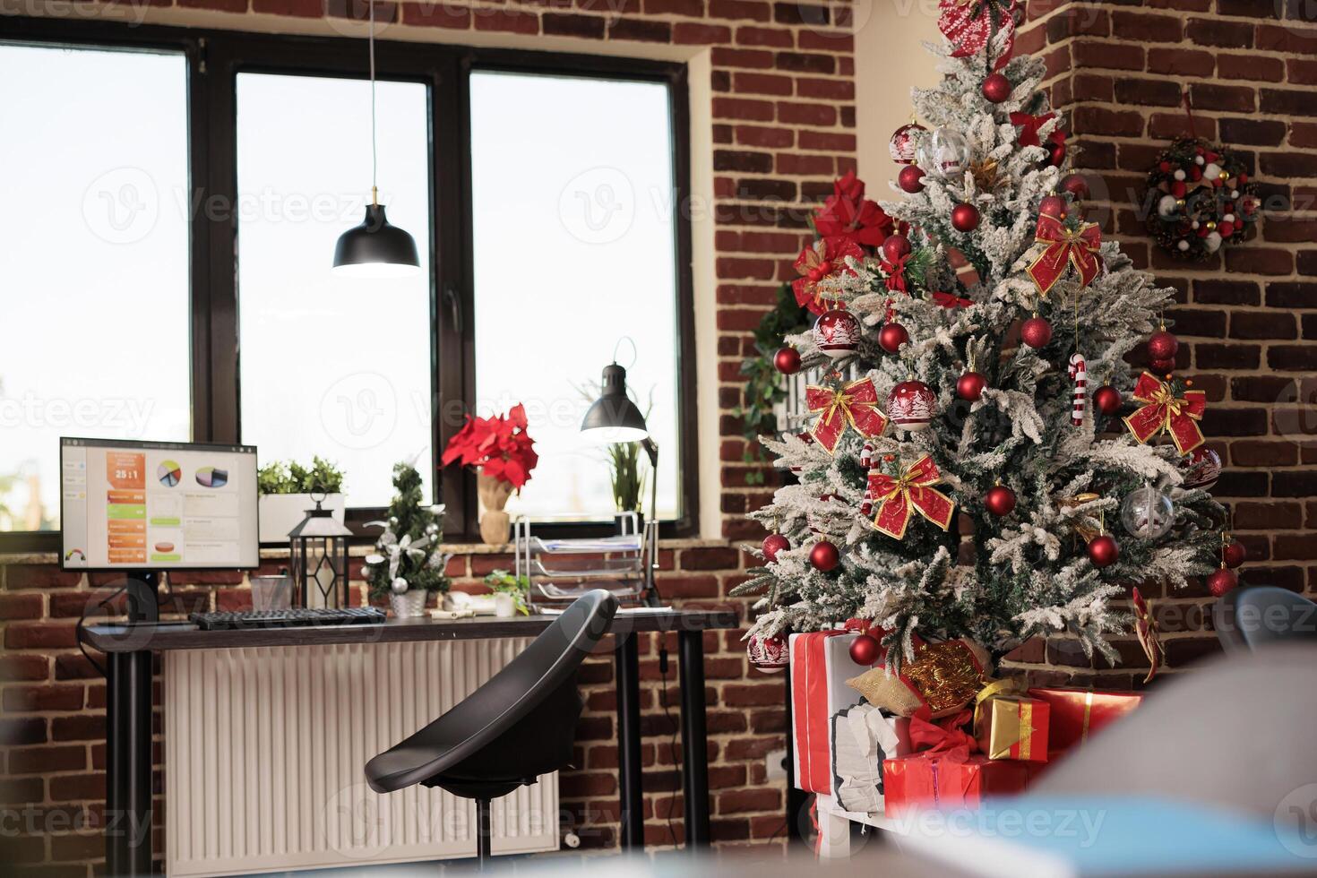 Decorated office workspace with festive christmas tree and presents during winter holiday season. Project statistics chart on computer screen at workplace during new year celebration photo
