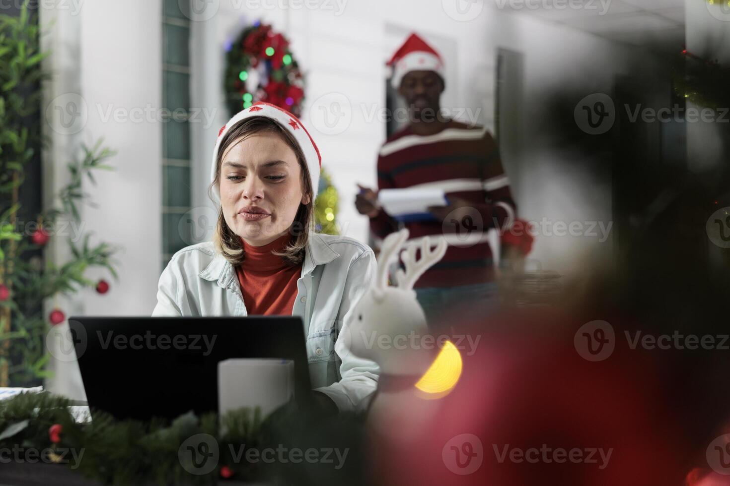 Employee working on company project with deadline approaching soon before winter holiday season. Worker solving tasks and finishing paperwork in festive decorated office during Christmas photo
