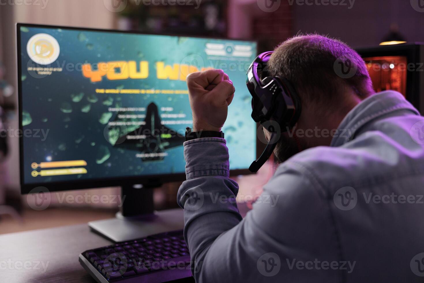 Gamer playing intense classic arcade spaceship racing videogame, clenching fist in excitement after winning. Joyful man having burst of happiness after passing game mission photo